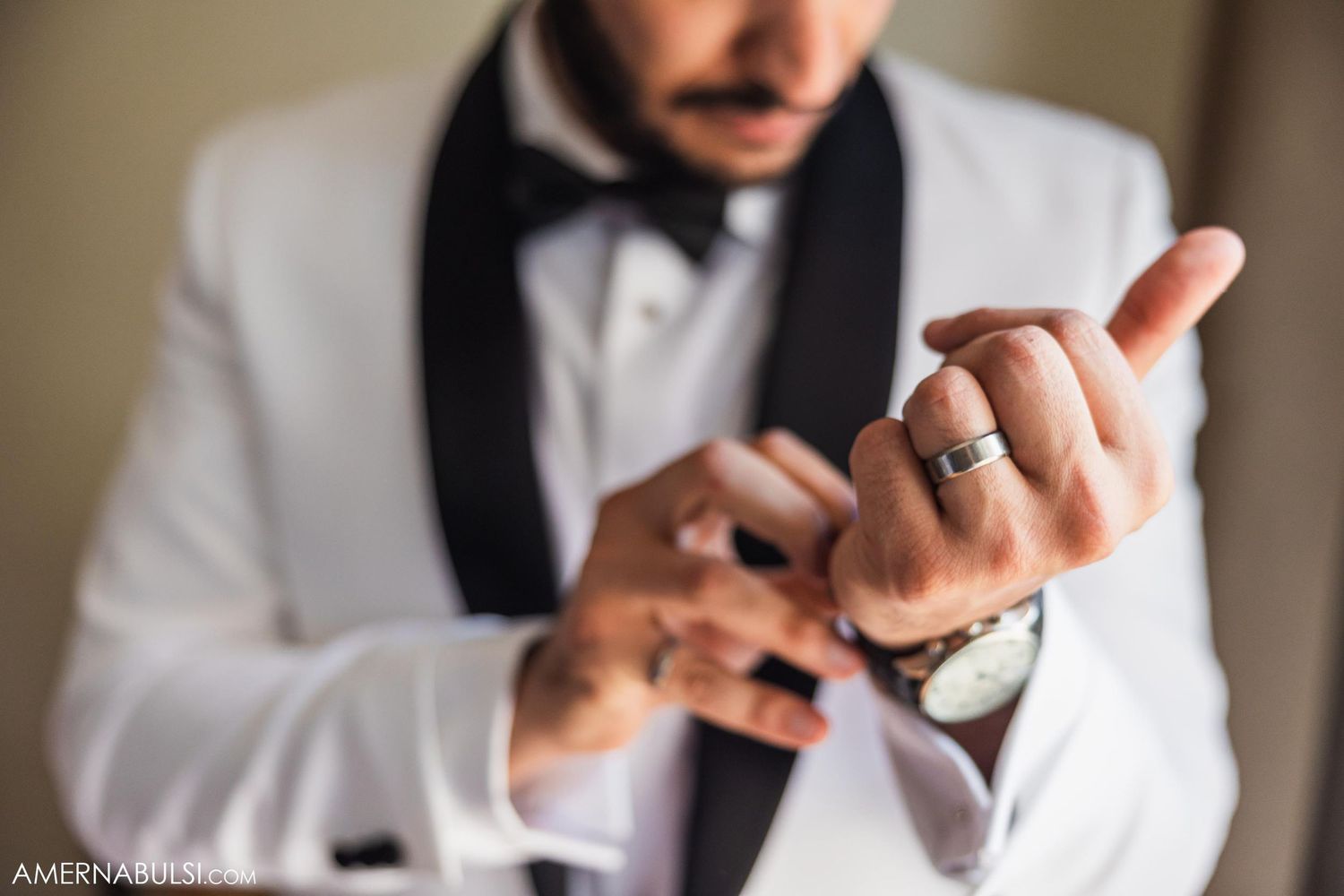 Hands adjusting cufflinks on a formal white tuxedo with black lapels.