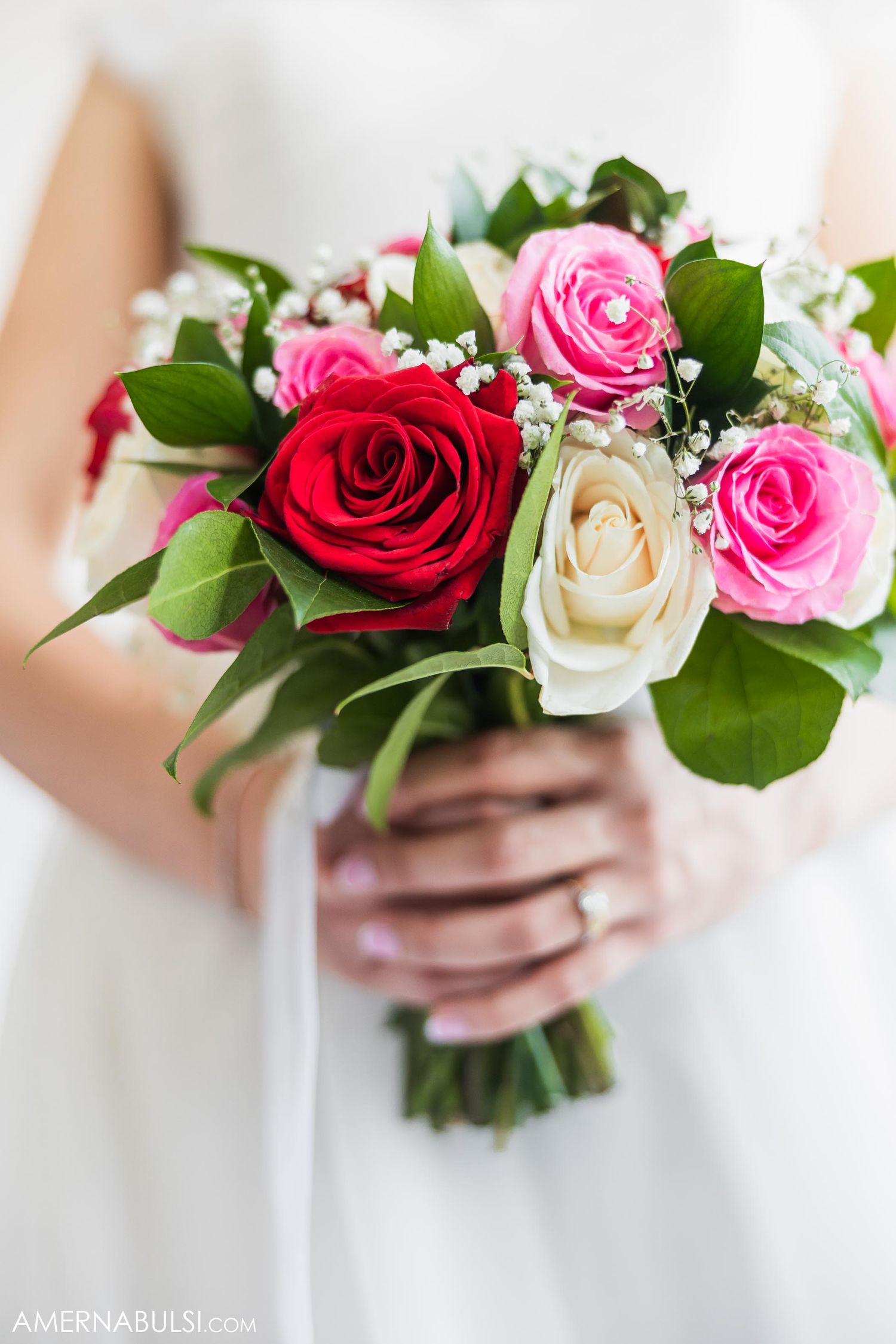 Beautiful bridal bouquet featuring red, pink and white roses with green foliage tied with white ribbon.