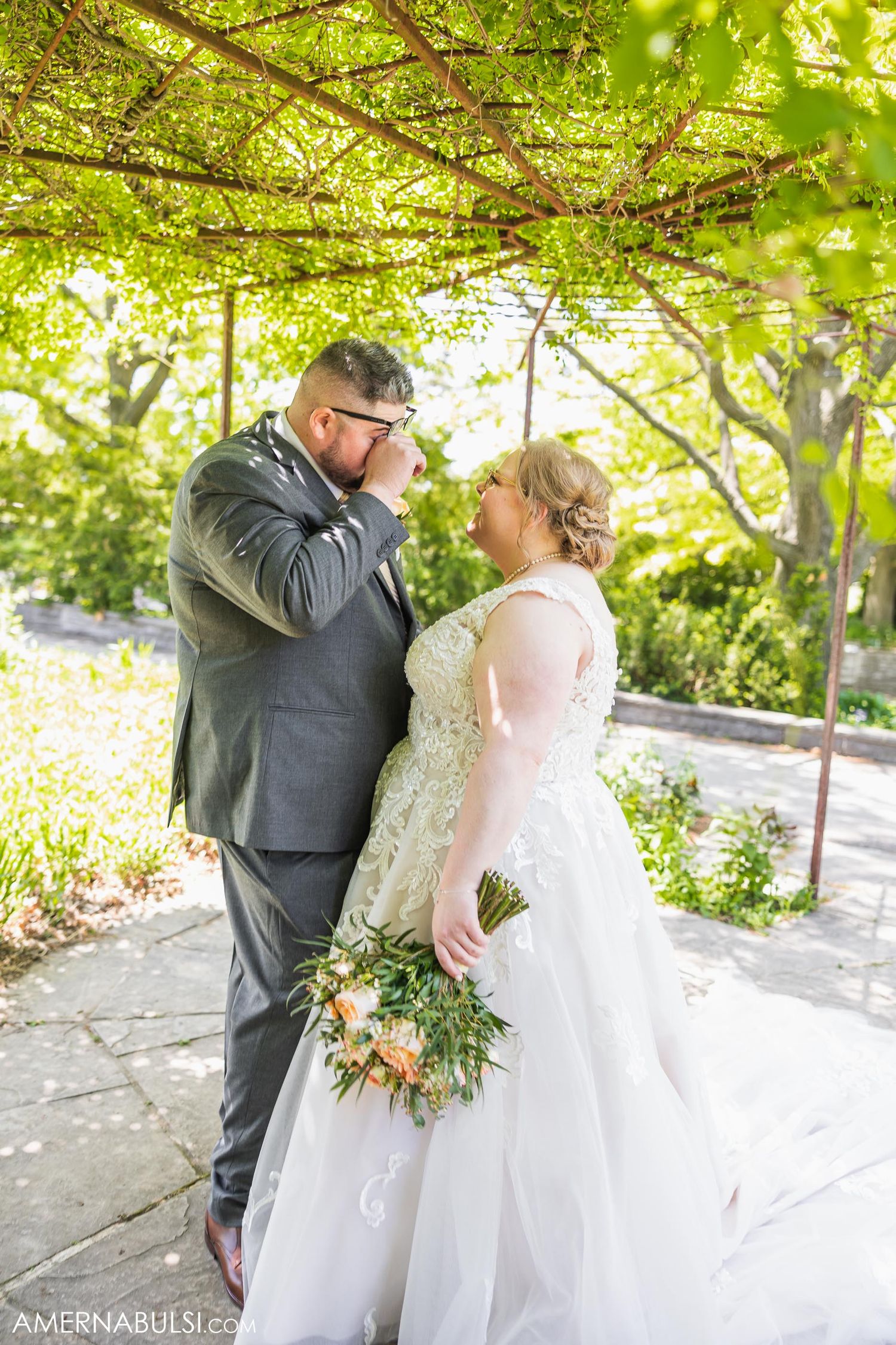 Tender wedding moment captured under natural vine covered arbor in garden setting.