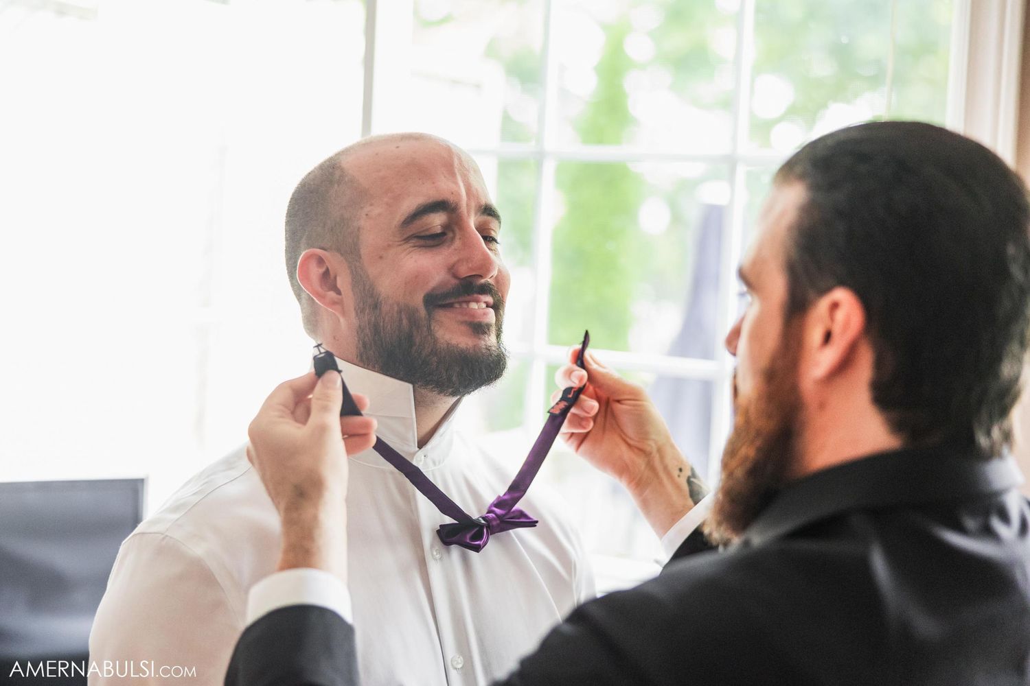 A bow tie being adjusted during formal wedding preparations in a sunlit room.