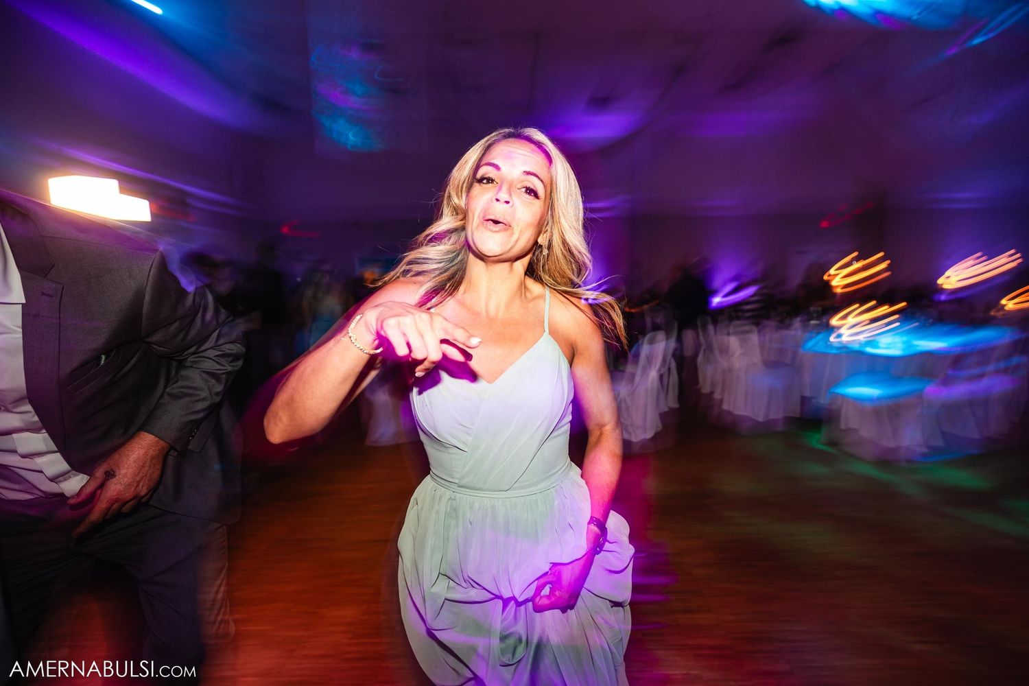 Wedding guest dances energetically under purple reception lighting.