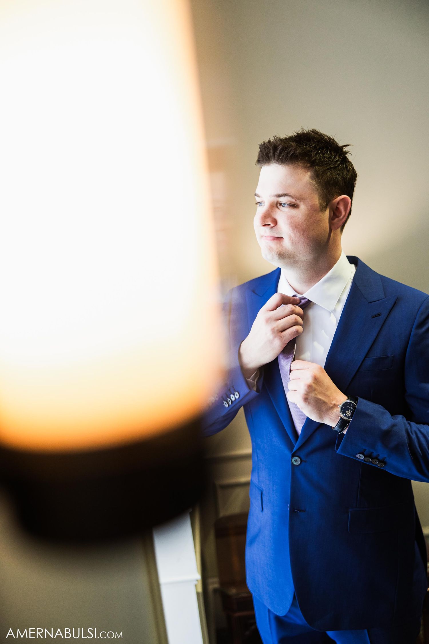 Person in blue suit adjusting tie while getting ready in warm natural light.