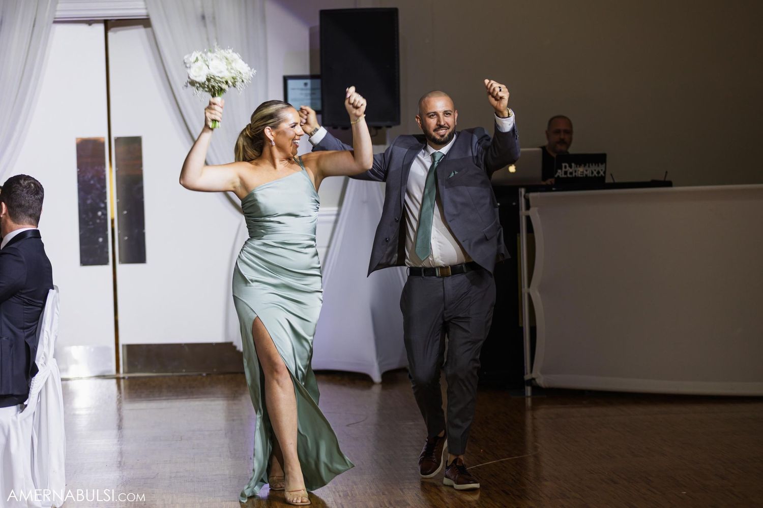 Elegantly dressed pair dance energetically at a wedding reception in coordinated celebration.