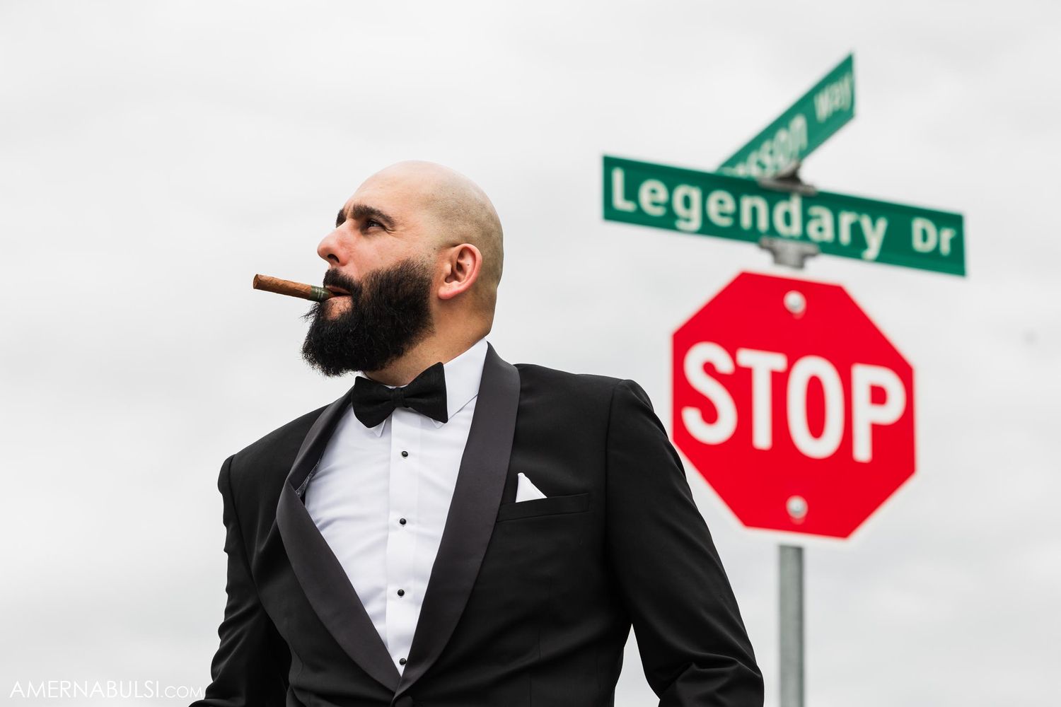 Person in tuxedo with cigar standing near street sign reading 'Legendary Dr' and stop sign.