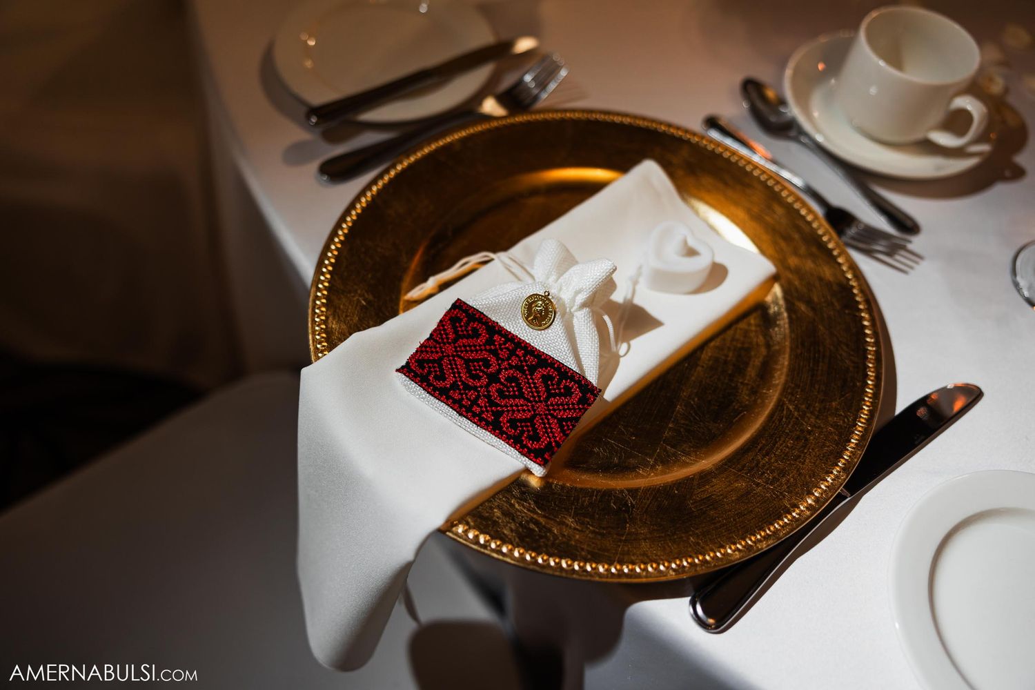 Elegant place setting with gold charger plate and red napkin details at wedding reception.