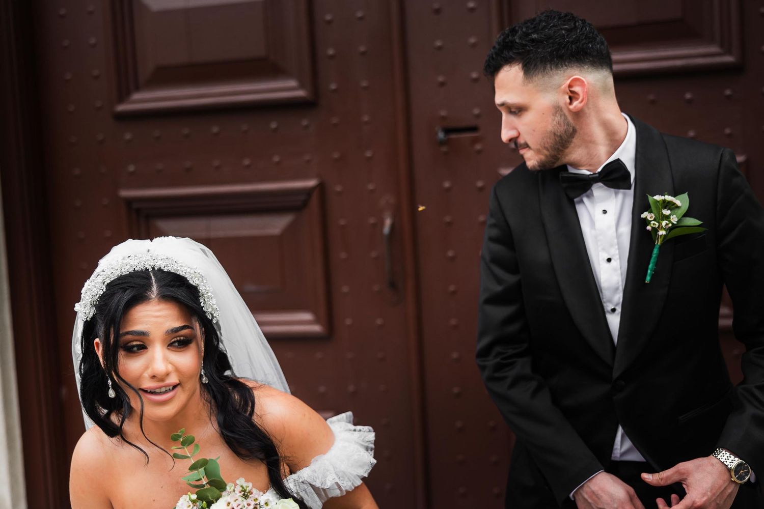 A candid moment during a wedding photoshoot outside an ornate wooden door.