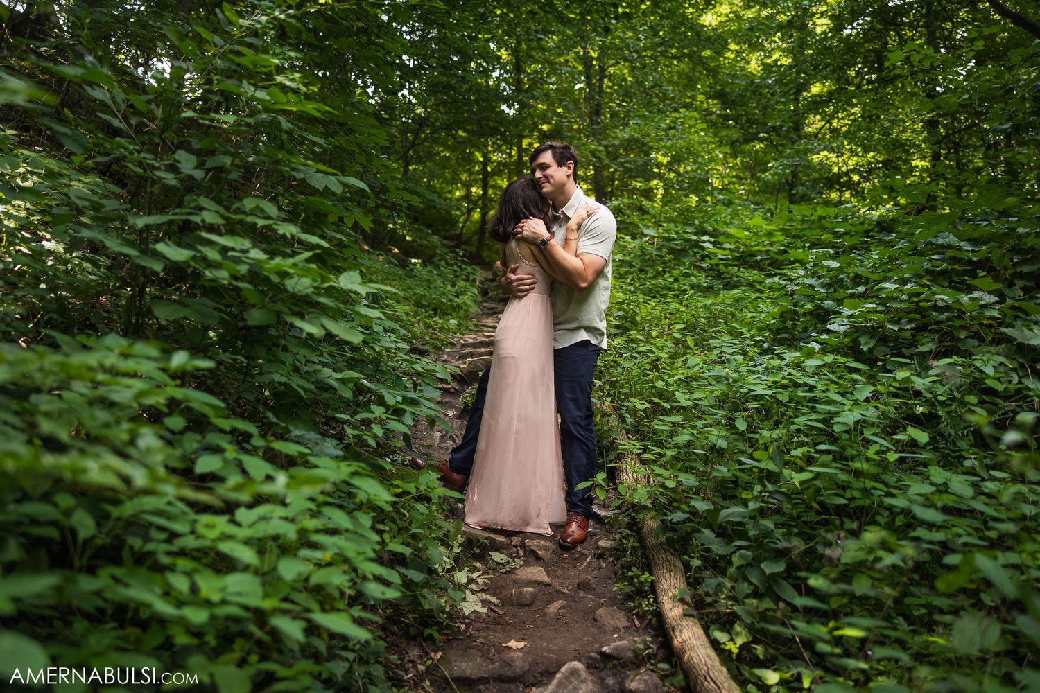 Couple shares romantic moment on forest trail surrounded by green vegetation.
