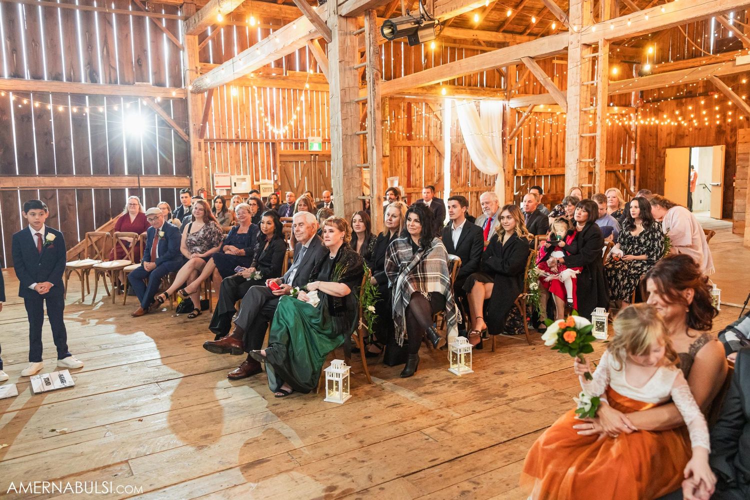 Wedding guests seated in rustic barn venue with string lights overhead.