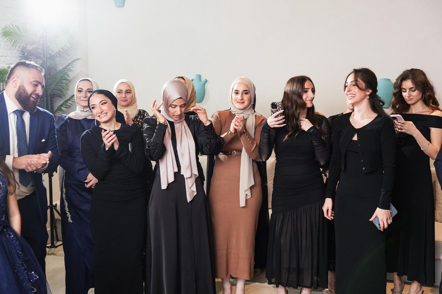 Wedding guests in formal attire gather together for a group photo at an indoor celebration.