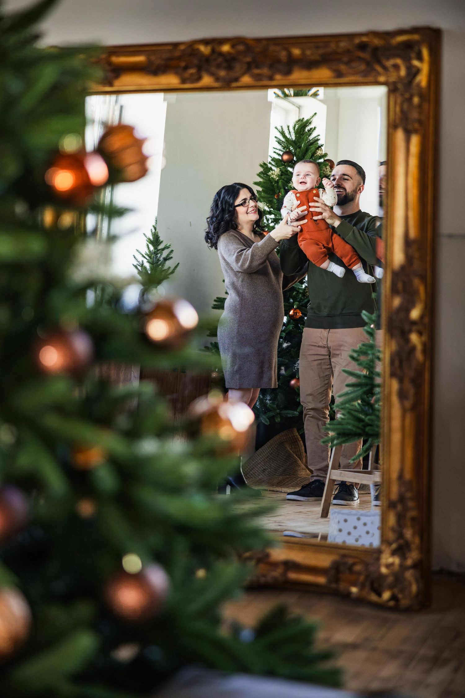 A family's reflection appears in an ornate gold mirror with Christmas decorations visible.