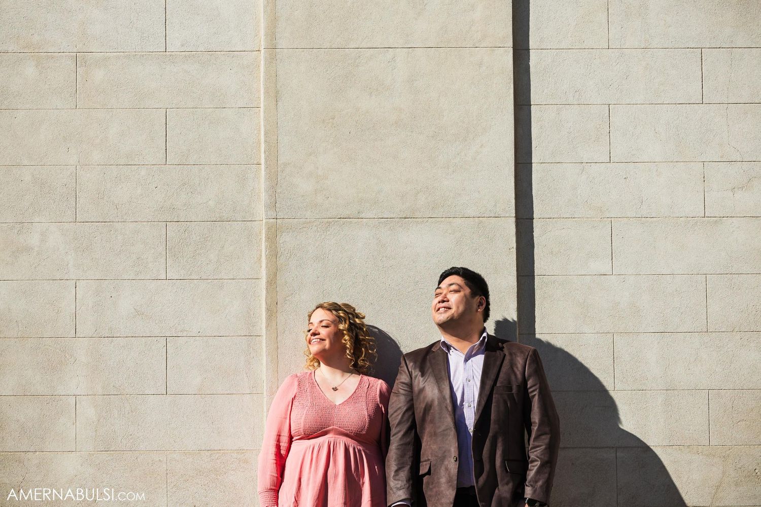 Couple leaning against stone wall casting dramatic shadows in bright sunlight.