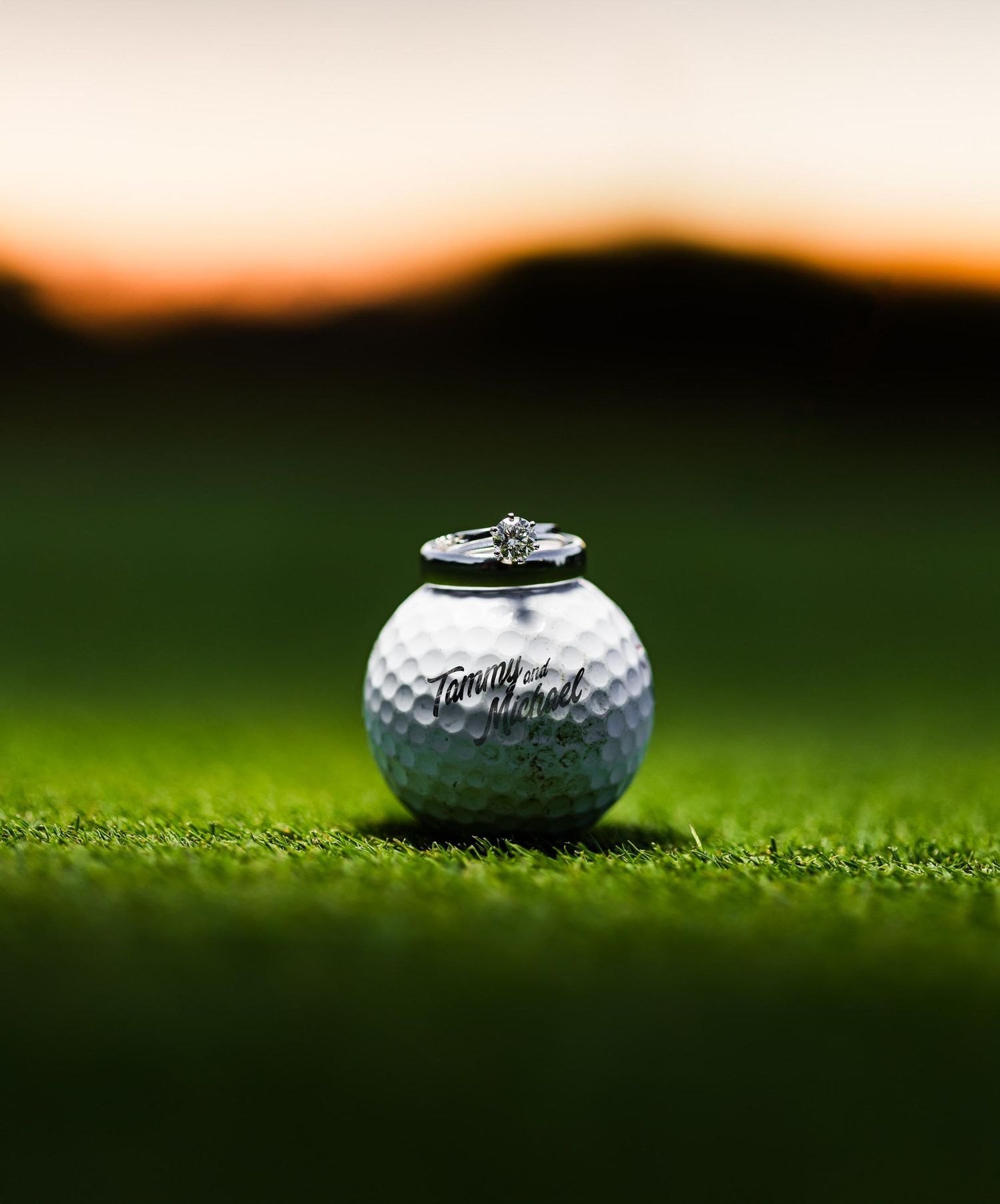 Wedding ring placed on golf ball against blurred sunset background.