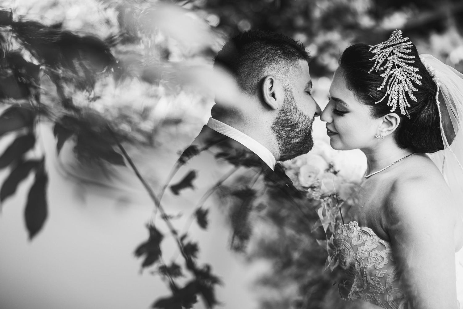 Intimate black and white wedding portrait with decorative headpiece and natural foliage.