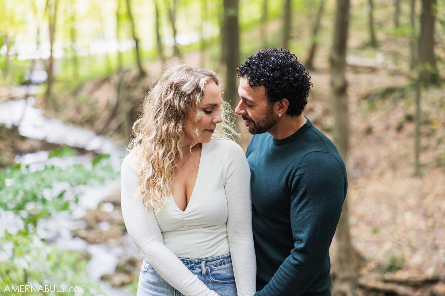 A couple laughs together while posing in a sunlit spring forest setting.
