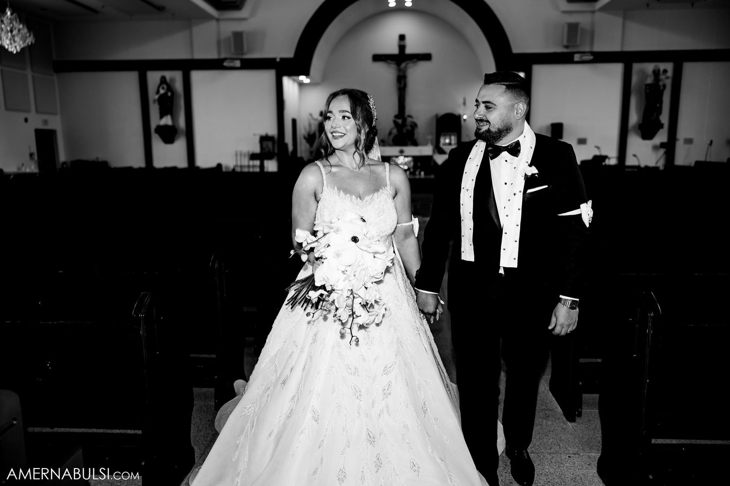 Black and white photograph of newlyweds walking down church aisle with beautiful architectural details.