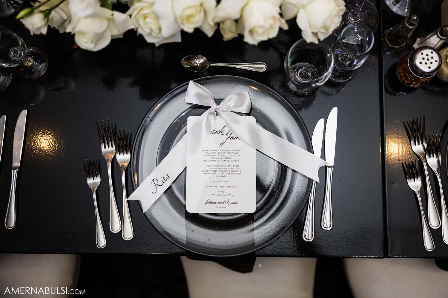 Elegant wedding table setting with white roses, black tablecloth, and silver place settings.