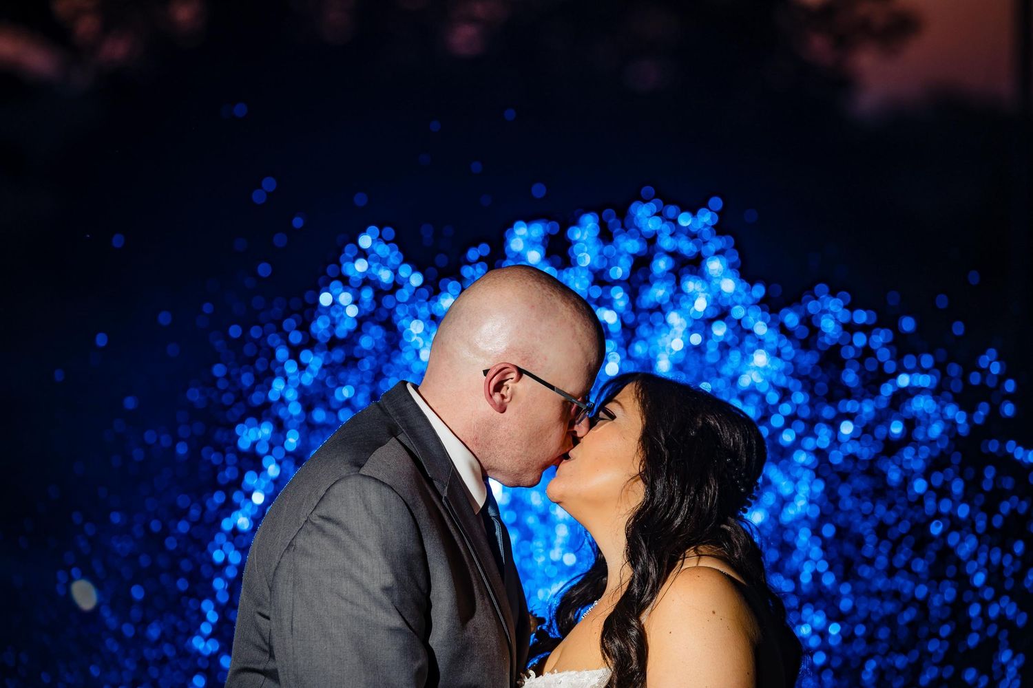 Romantic kiss captured against background of glowing blue bokeh lights.