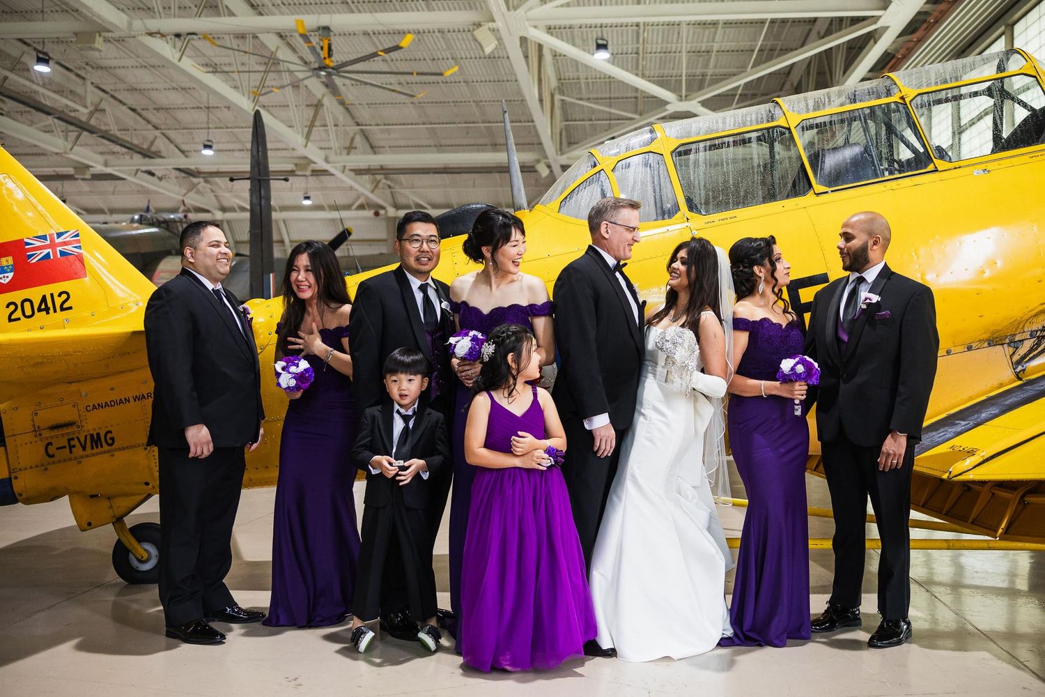 Wedding party poses with vintage yellow airplane in aviation museum.