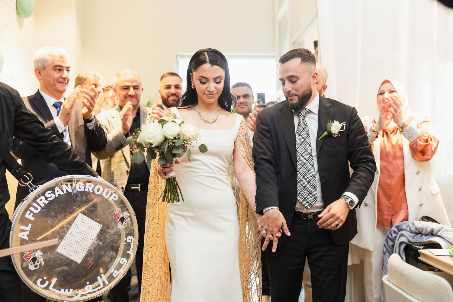 Newlyweds making their grand exit while guests cheer and applaud in a decorated venue.
