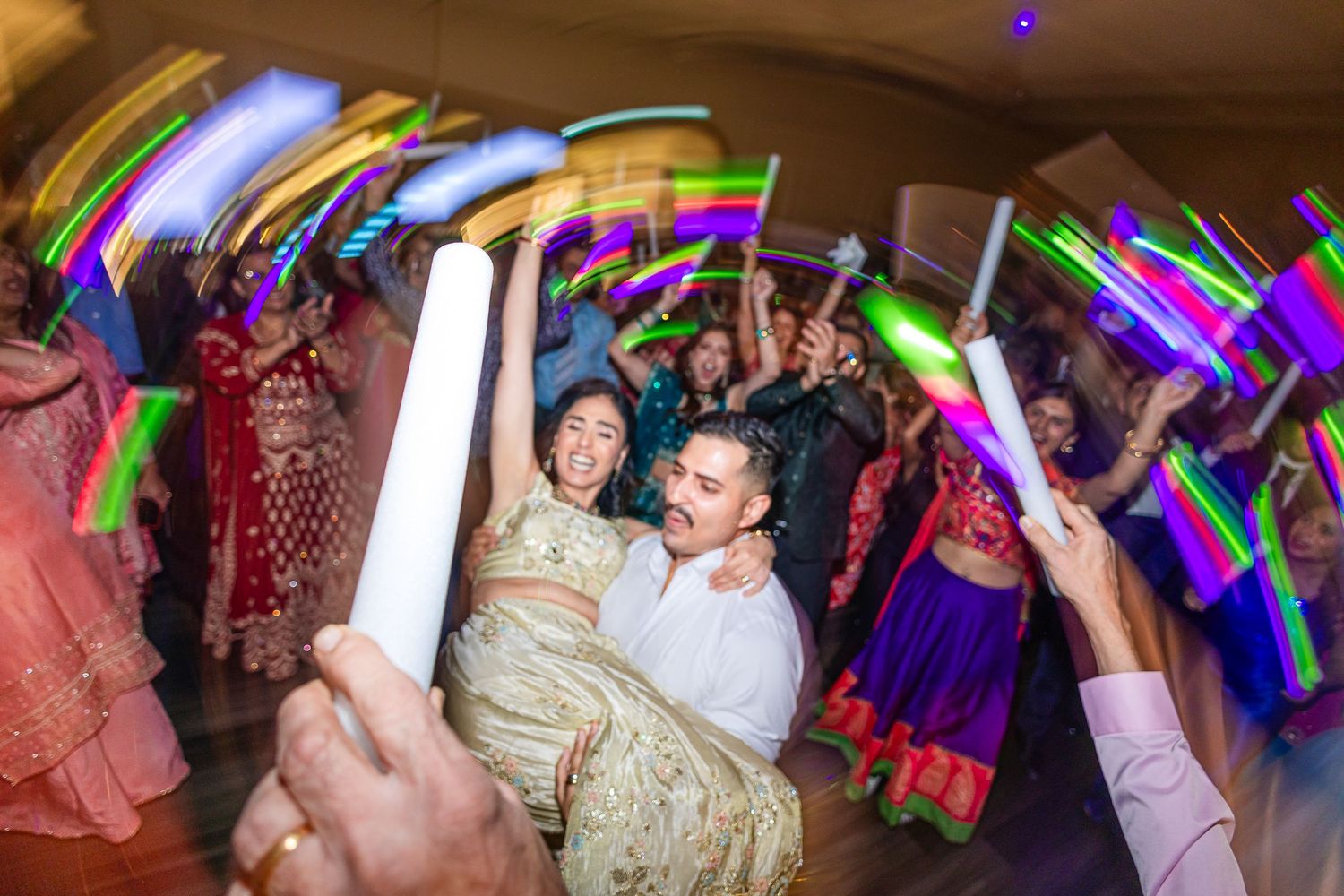 Colorful LED foam sticks wave through the air as party guests dance and celebrate at a lively nighttime event.