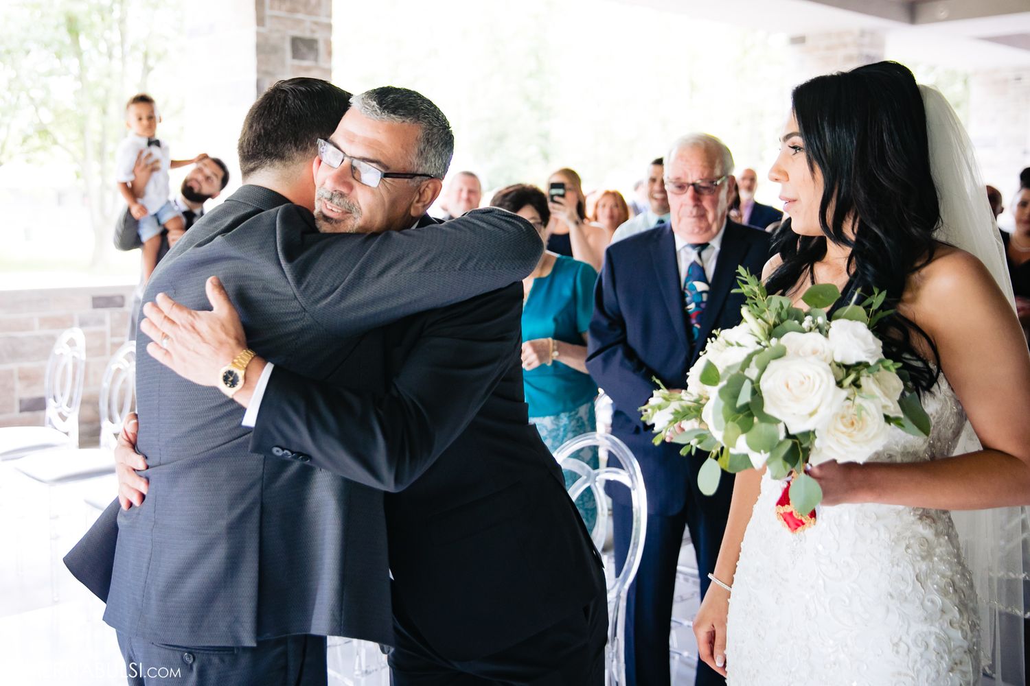 Wedding guests embrace and celebrate during an emotional reception moment at an indoor venue.
