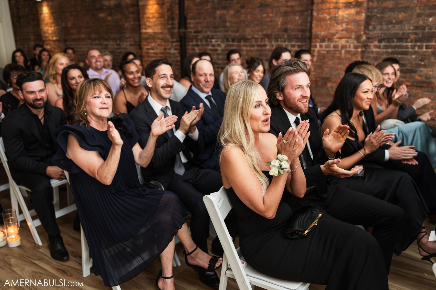Wedding guests clapping and showing emotion during ceremony in rustic brick venue.