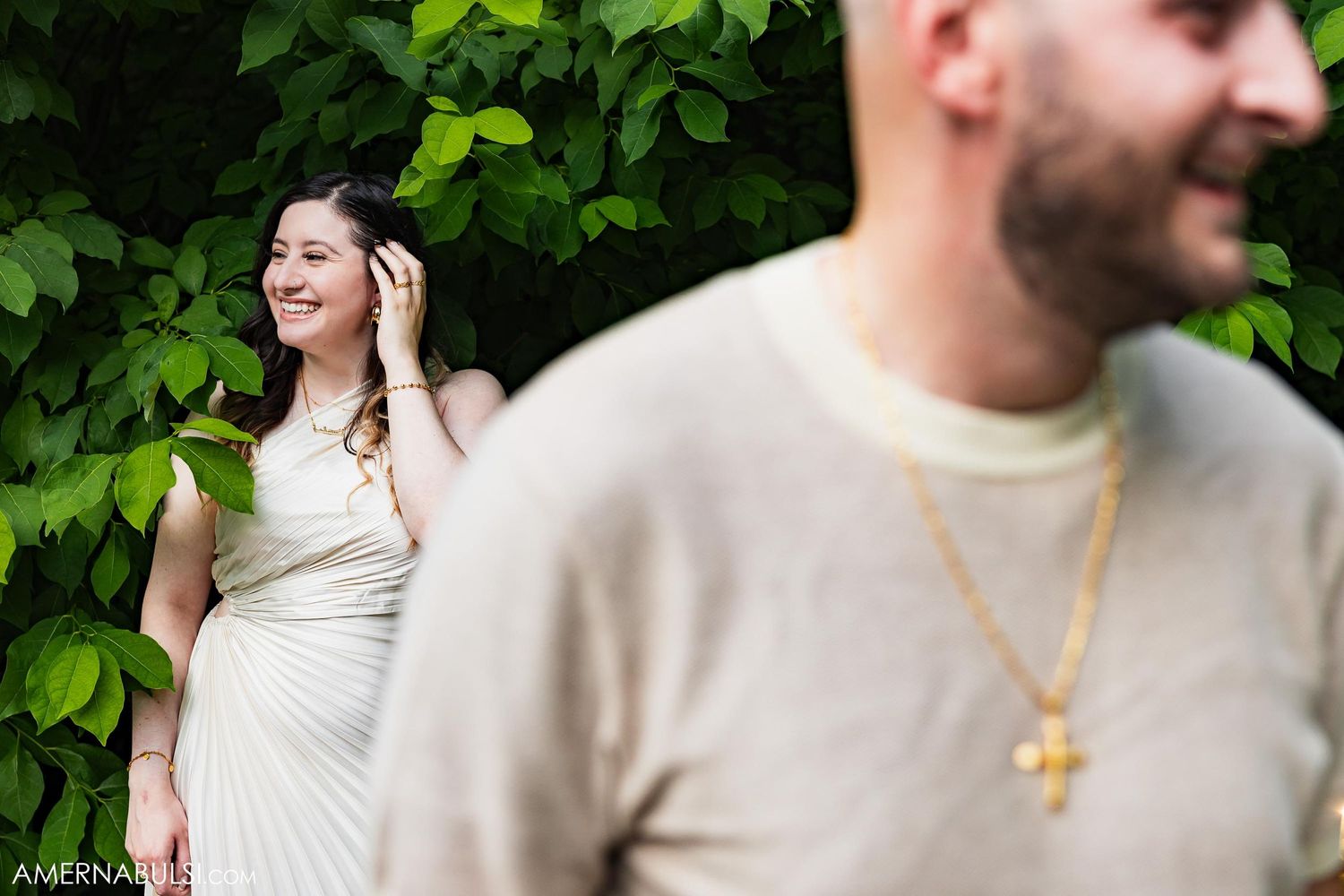Candid shot of couple in casual attire against green foliage background.