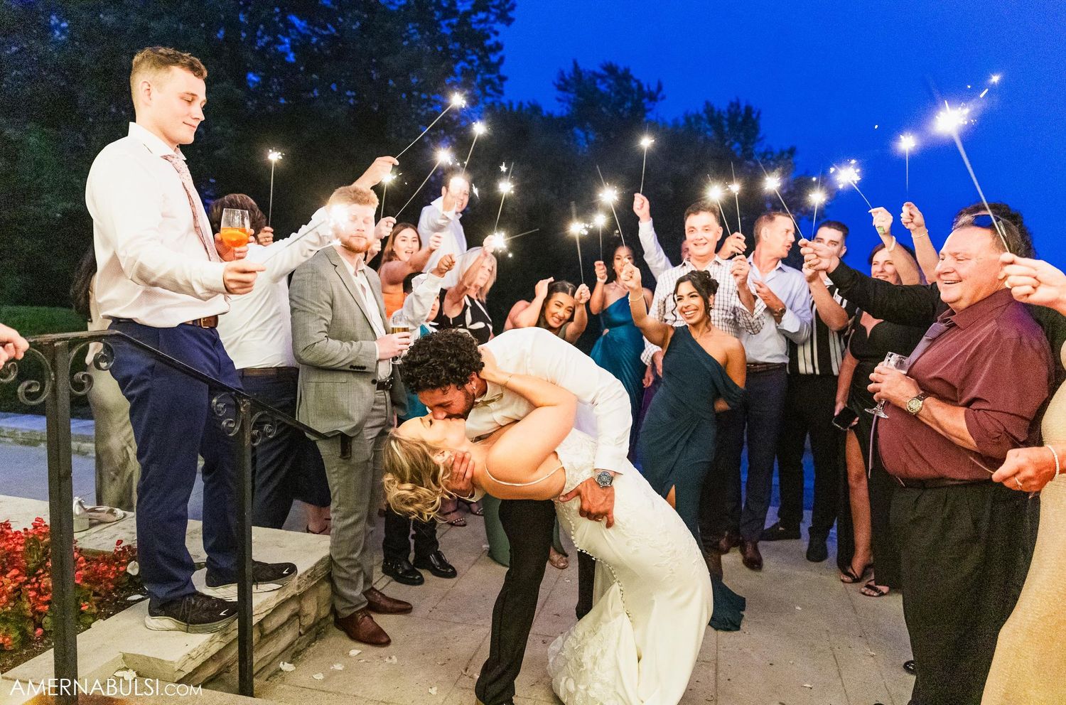Wedding guests hold sparklers during celebratory nighttime send-off.