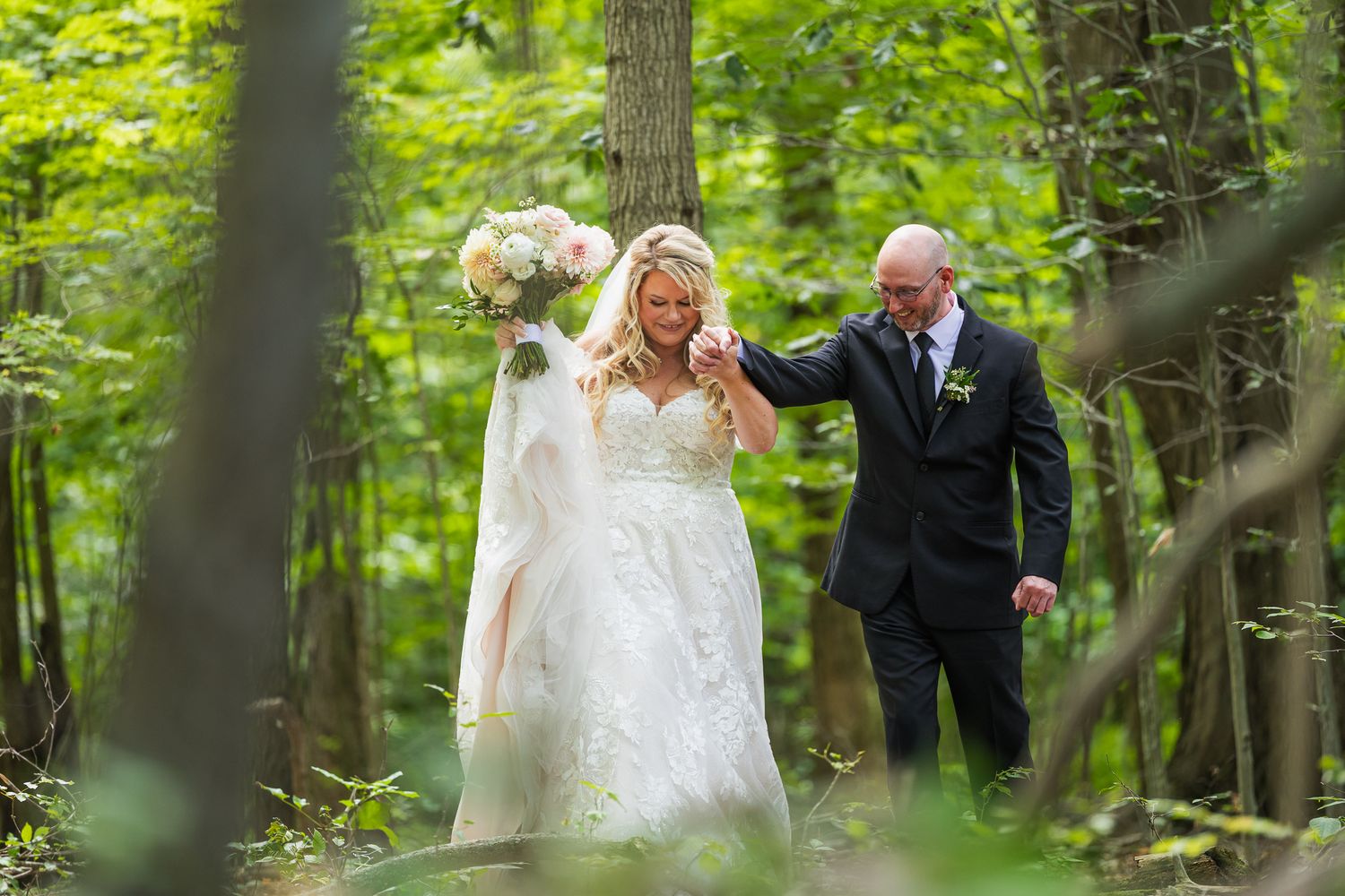 Wedding party walking through lush green forest setting in formal attire.