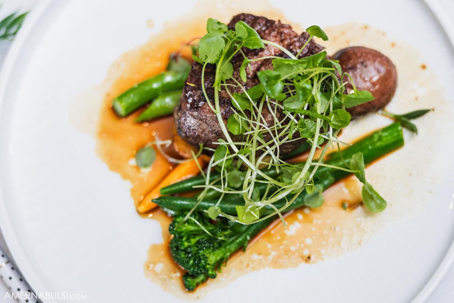 Gourmet plated steak with microgreens and asparagus in a light sauce.