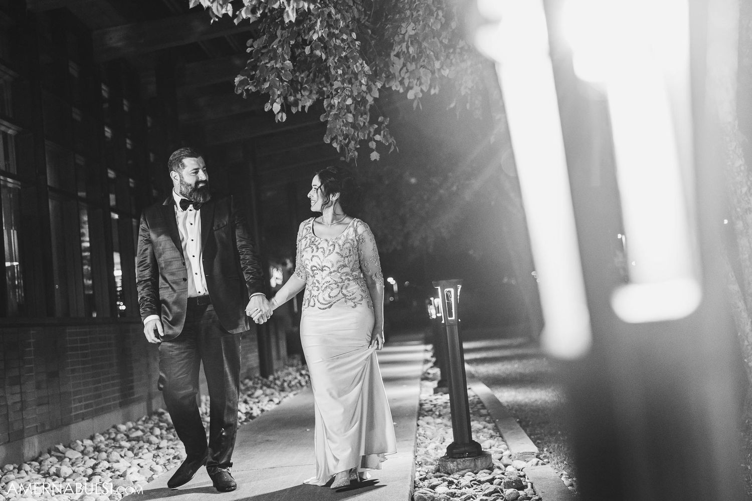 Couple walks together on tree-lined path in formal wedding attire.