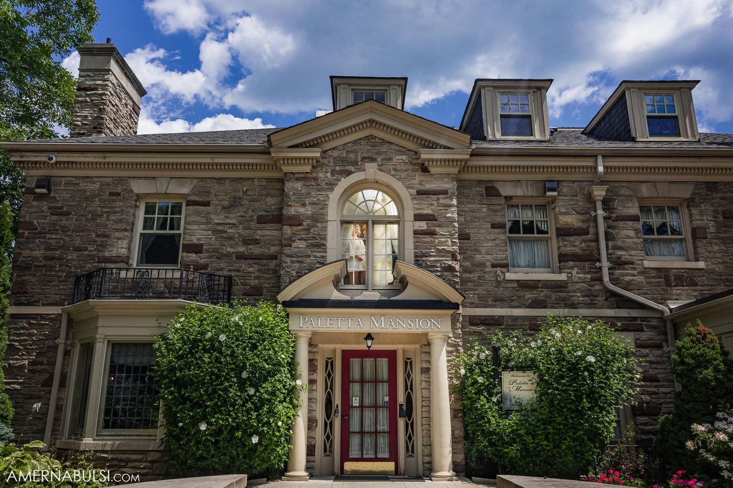 Elegant stone mansion with dormer windows and ornate entrance features classical architectural details and climbing vines.