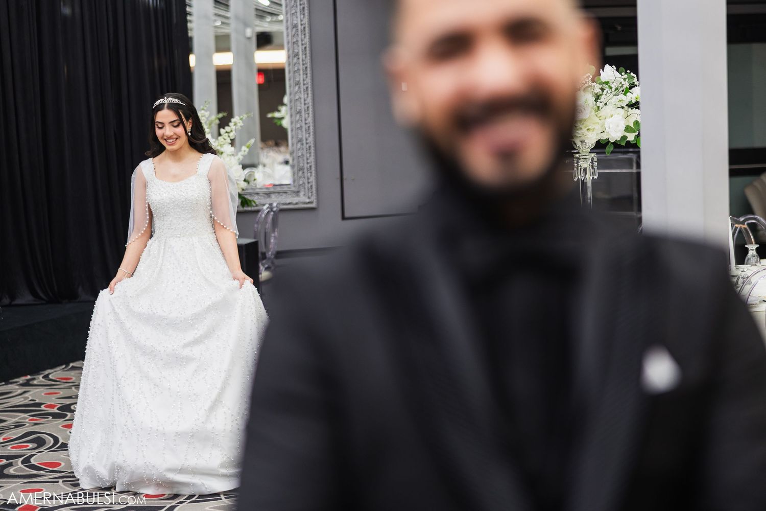 A bride in a white wedding dress sits on a wooden bench in an elegant outdoor setting.