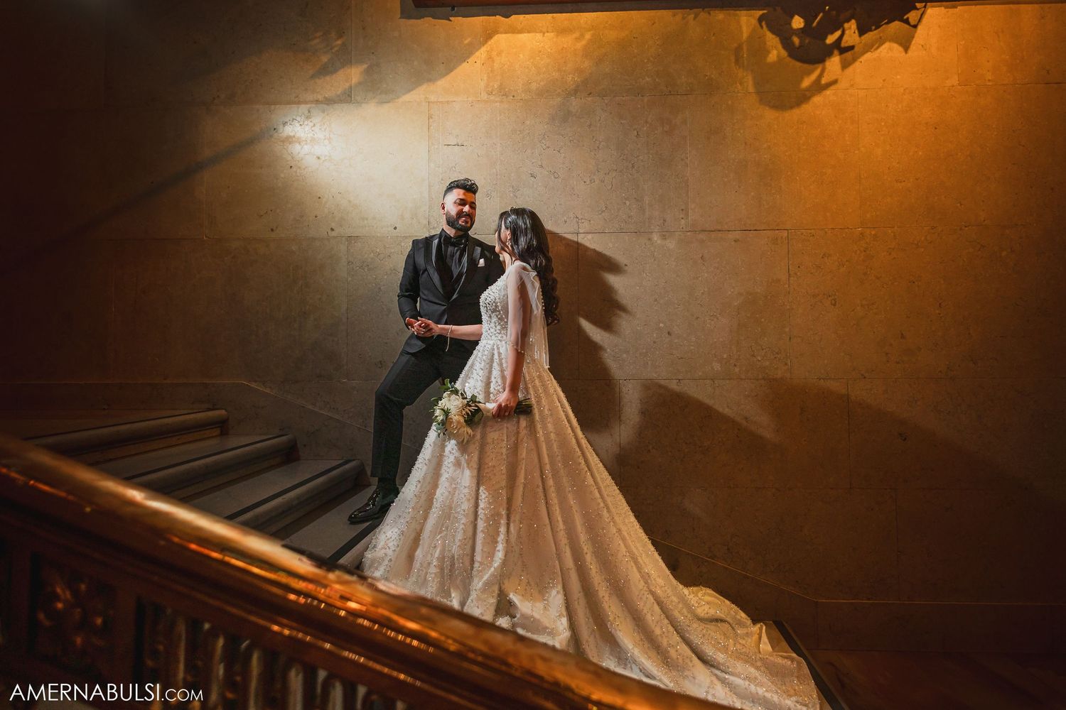 A dramatic wedding portrait of a couple on a staircase with moody lighting and shadows.