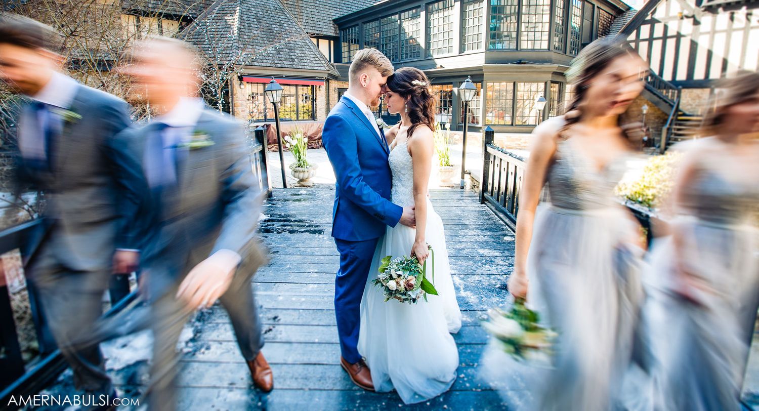 Wedding couple sharing intimate moment as guests blur past in motion on outdoor deck.