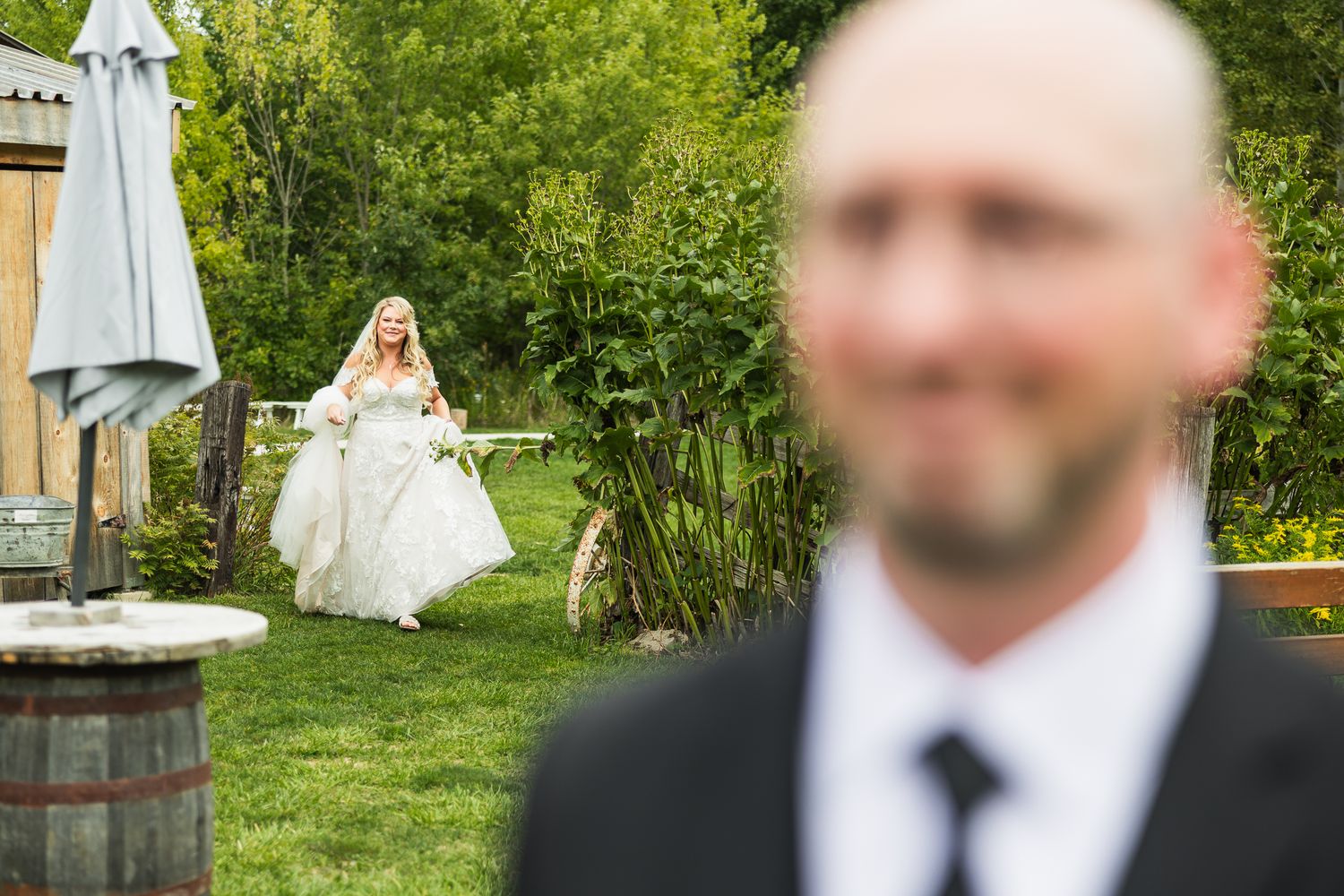 Newlyweds share intimate moment during outdoor garden ceremony with white parasol in background.