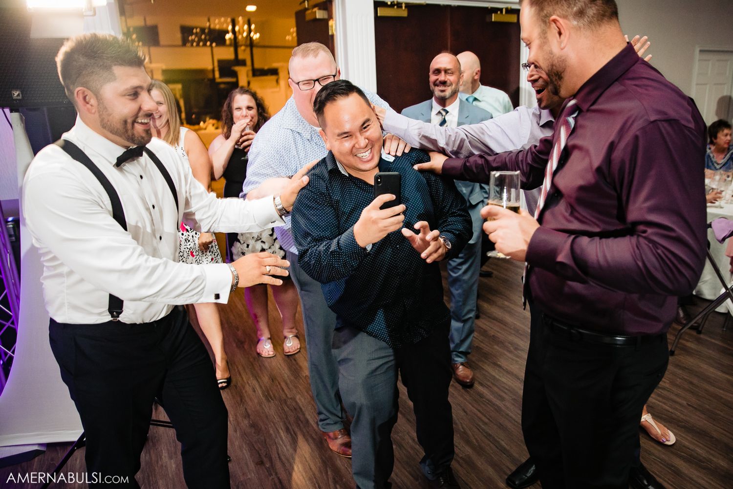 People in formal attire laughing and socializing at an indoor event with warm lighting.