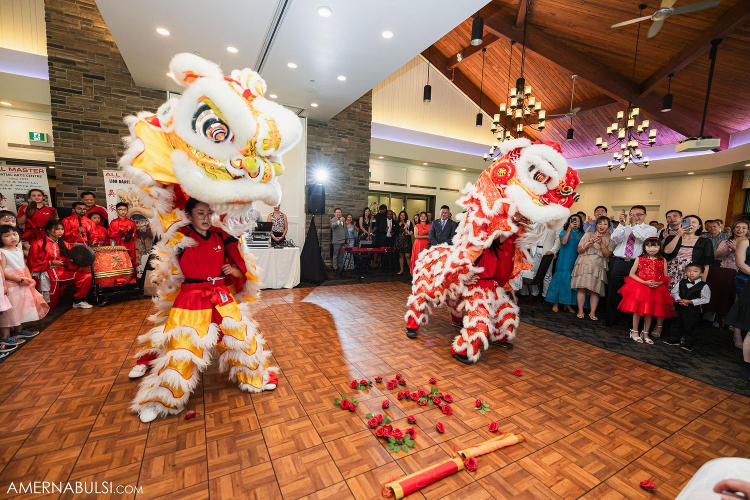 Colorful lion dance performers entertain guests on wooden dance floor at wedding celebration.