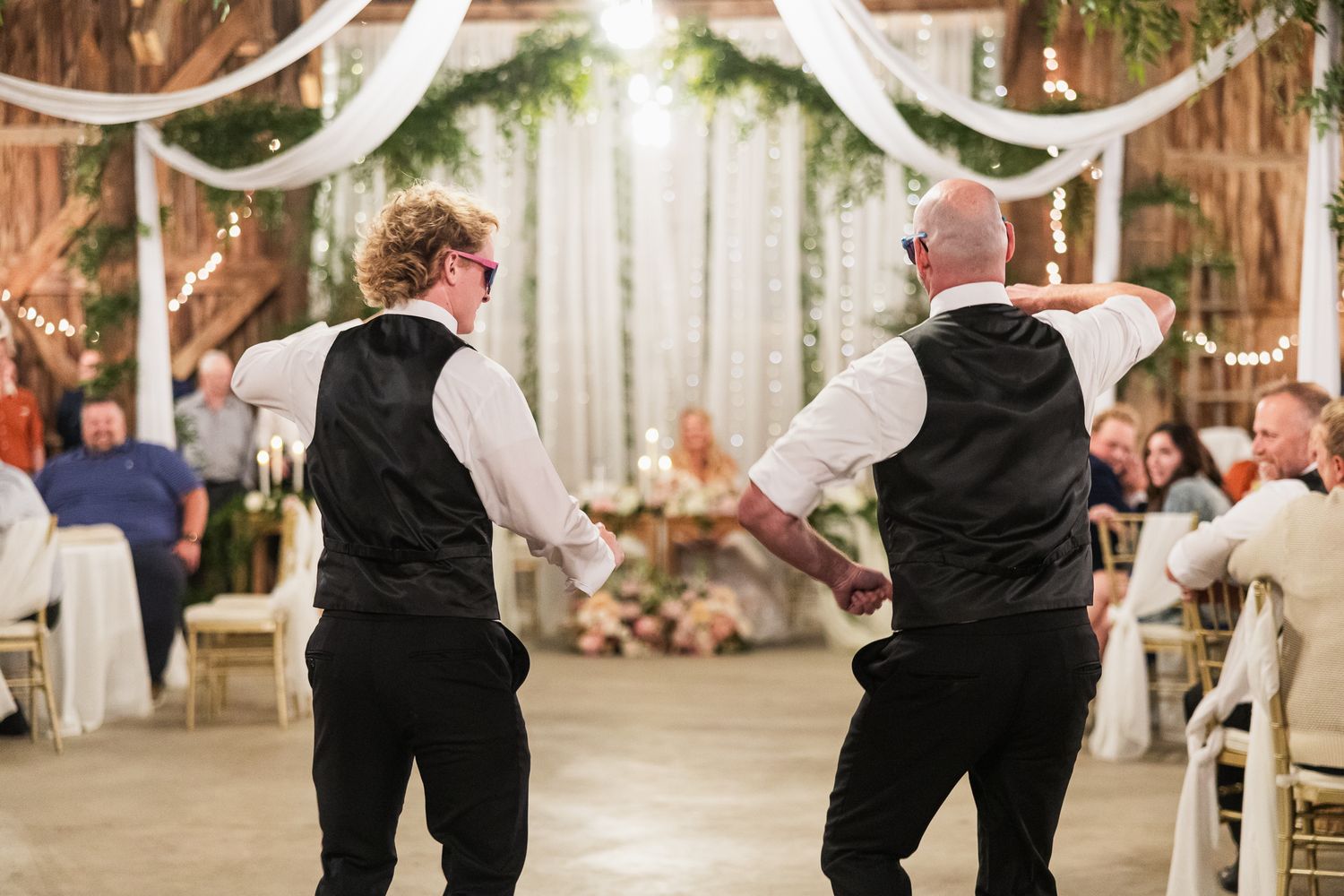 Elegant barn wedding reception space decorated with white drapes and greenery for dancing.