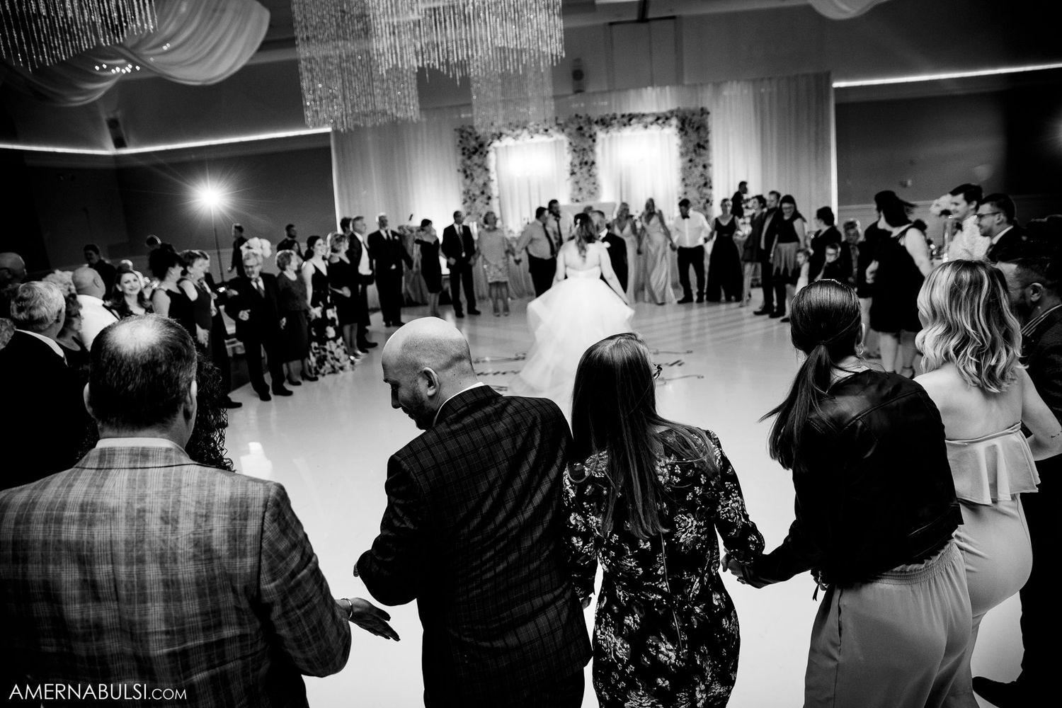 Black and white photo of wedding guests dancing in a circle during reception.