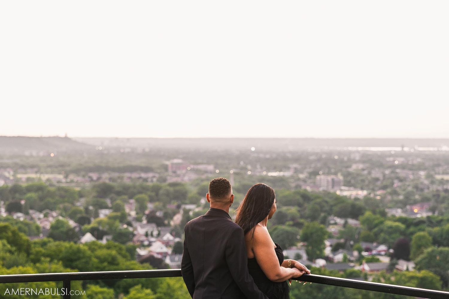 Couple sitting on observation deck railing overlooking suburban landscape at dusk.
