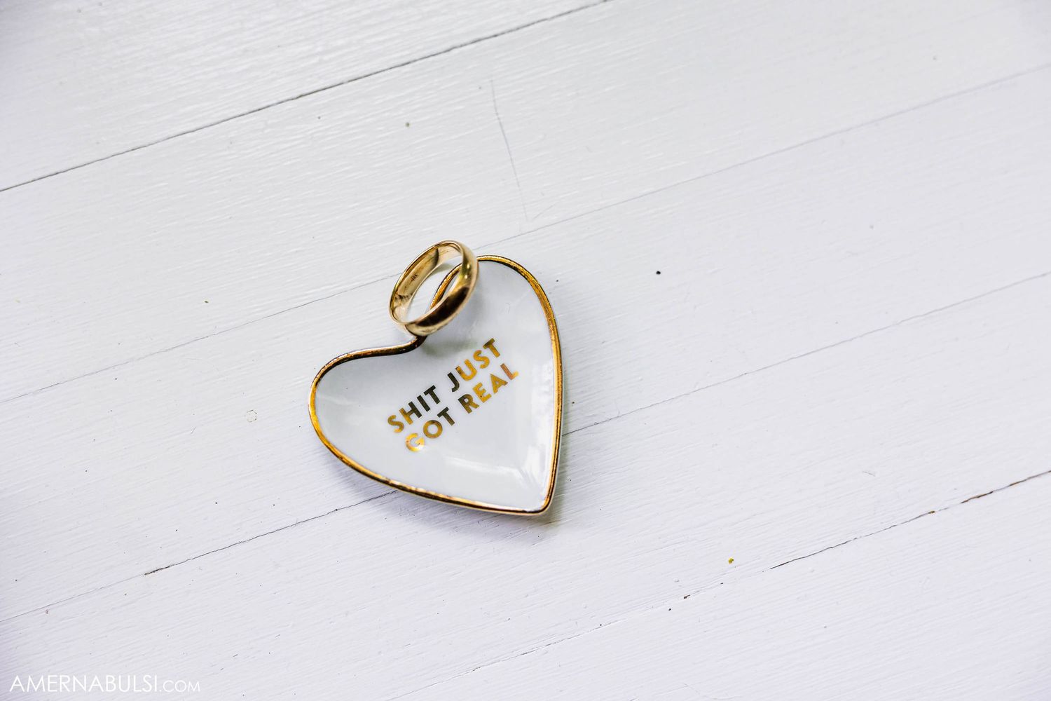 Gold wedding rings arranged in heart shape on white surface with text inside.