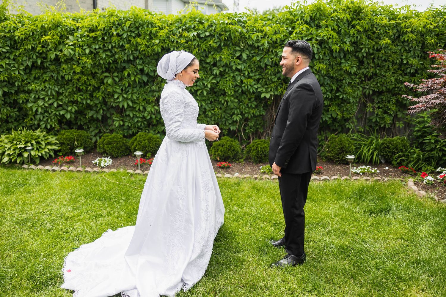 Wedding couple standing together on grass with hedge background during outdoor ceremony.