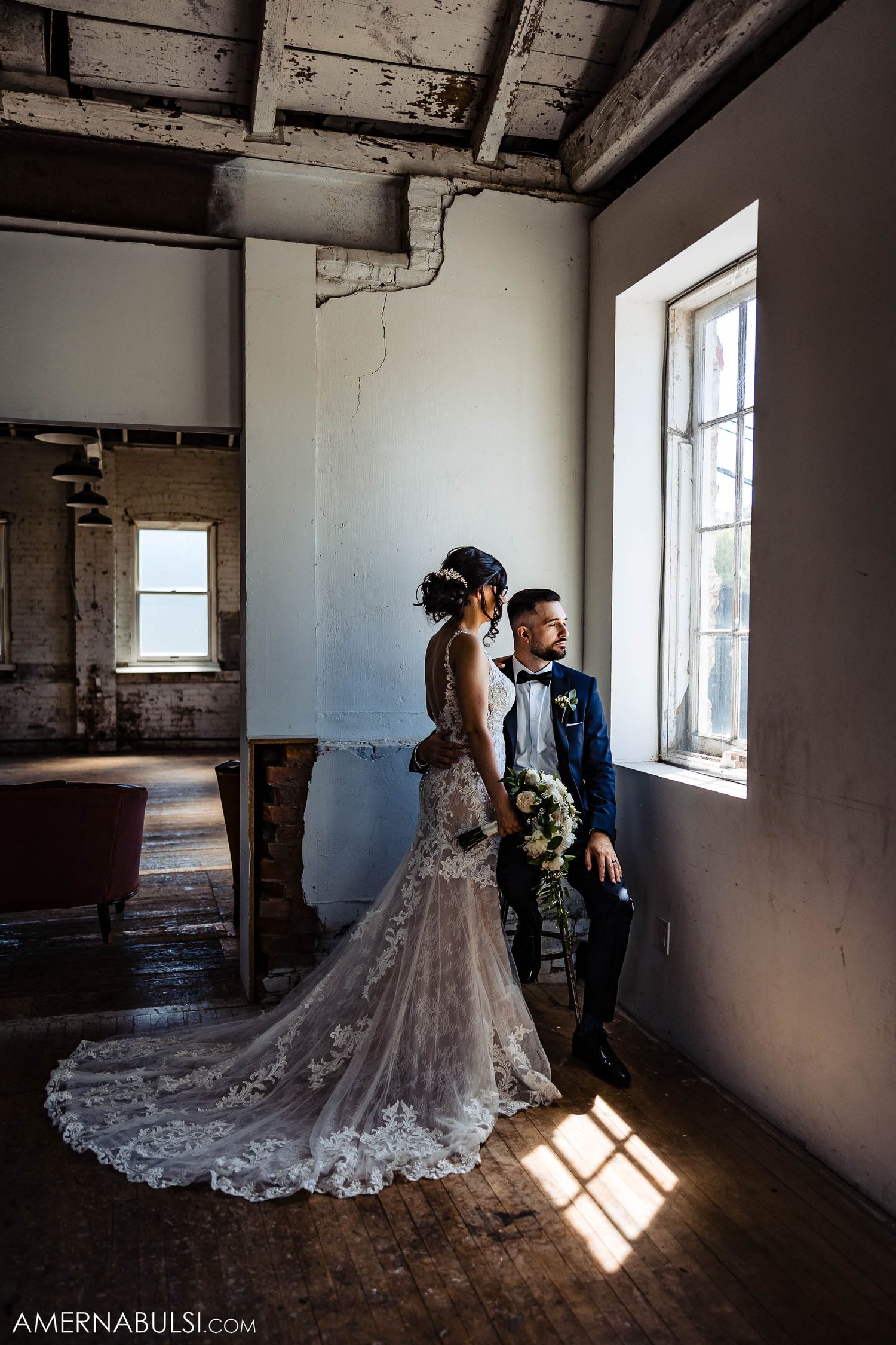 Artistic wedding photo of a couple standing in sunlight streaming through windows in an industrial space.