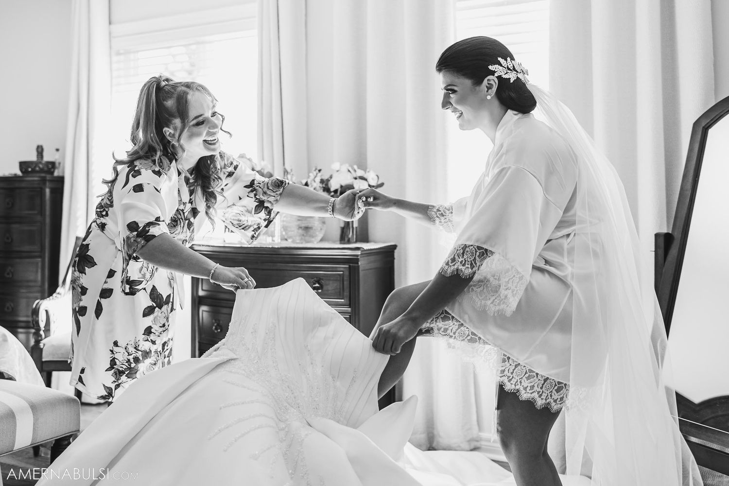 Two people in robes share a quiet moment while preparing with wedding dress visible.