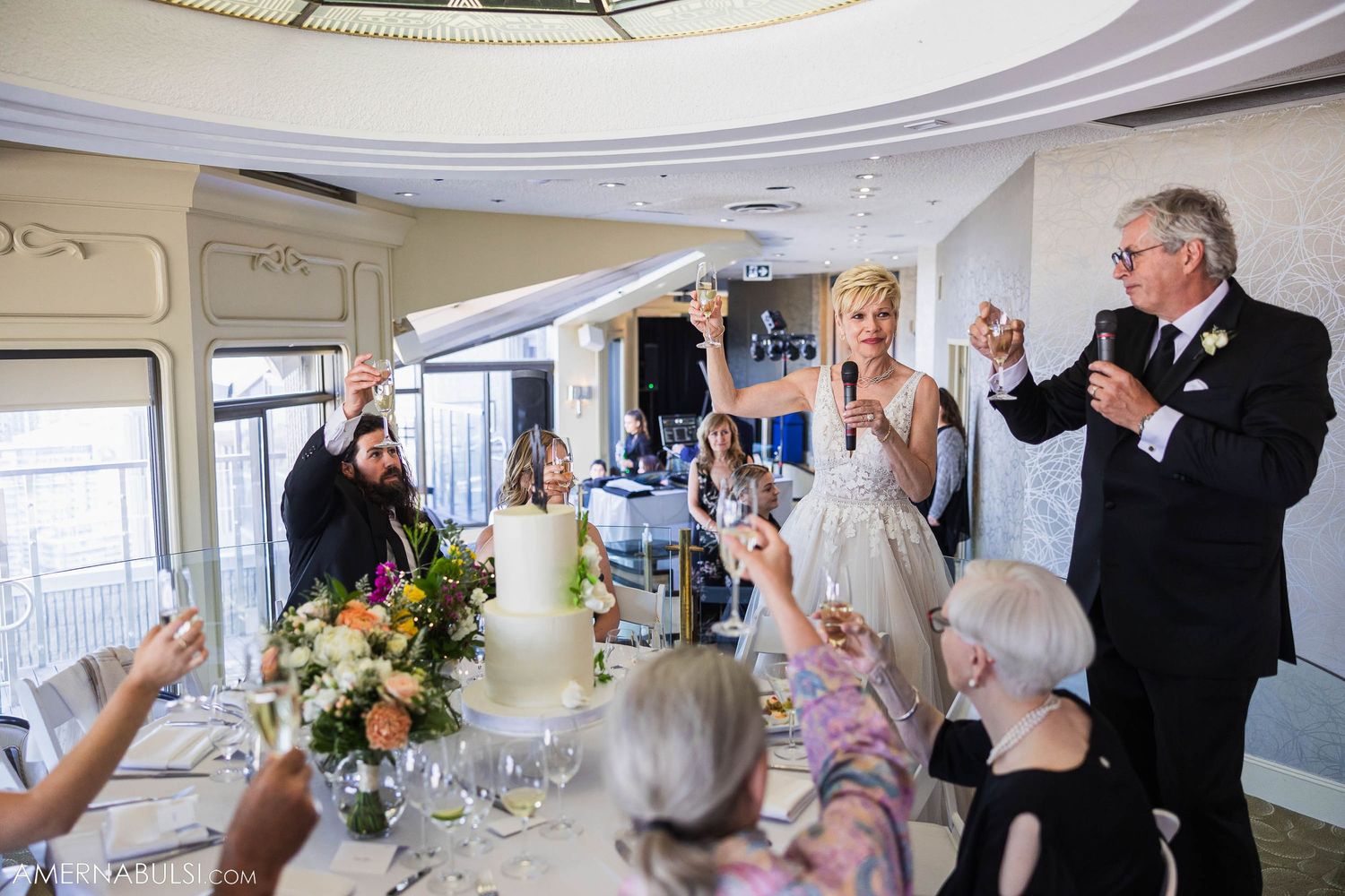 Wedding reception celebration with guests raising glasses for a toast in an elegant venue.