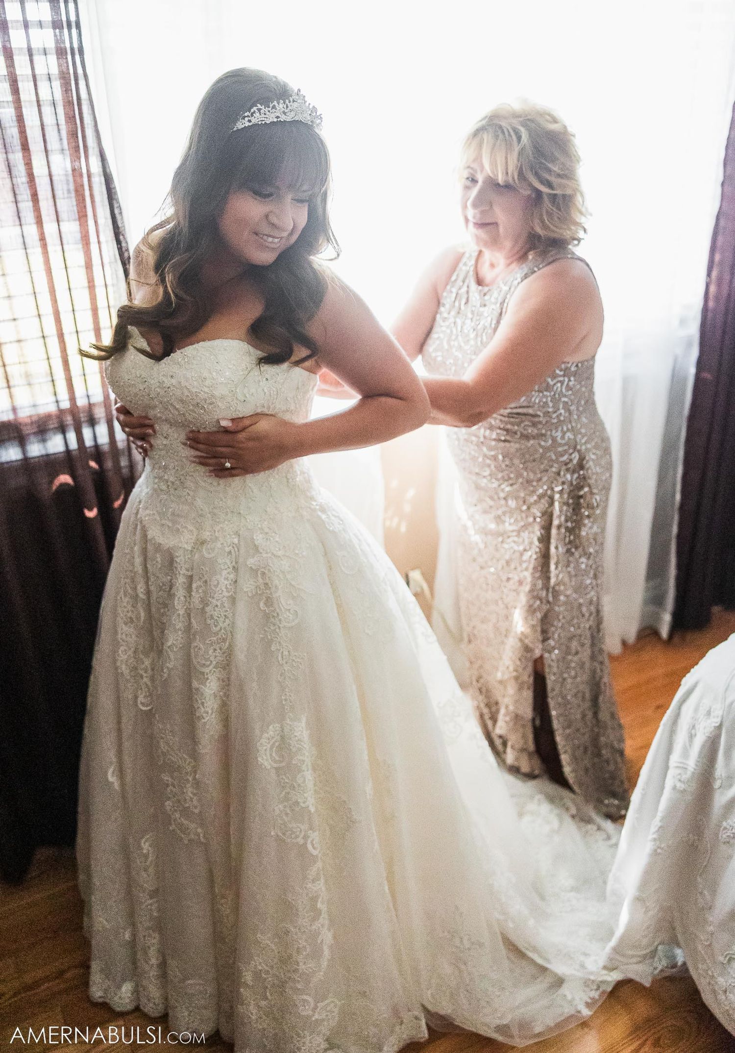 A tender moment during wedding preparations as a bride gets help with her lace wedding gown.