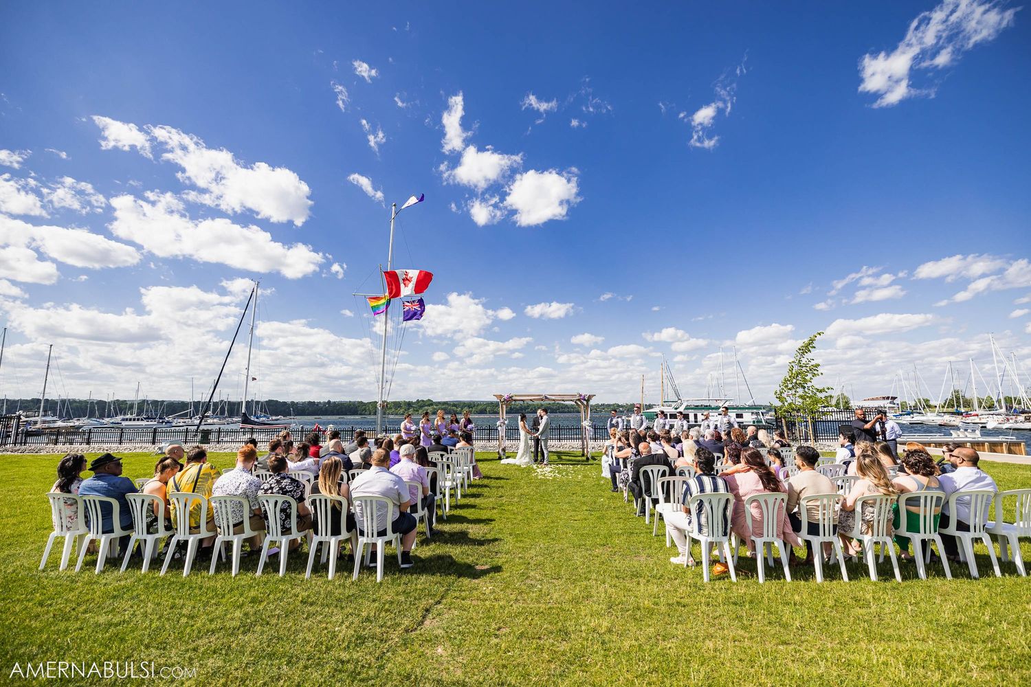 Outdoor wedding ceremony setup with white chairs and red balloons against blue sky.