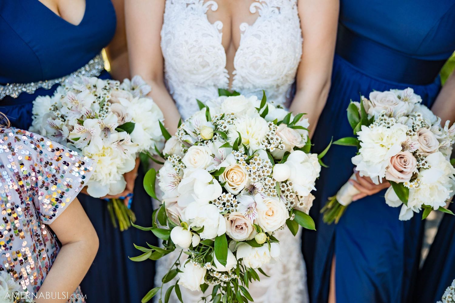 White and blush wedding bouquets held against navy blue bridesmaid dresses.
