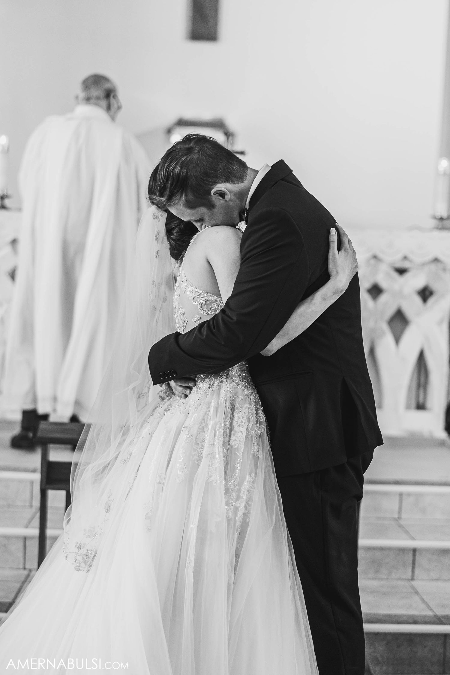 A black and white photo captures a tender moment between newlyweds at the church altar.